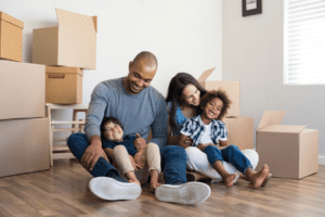 A family sits on the floor in front of moving boxes.