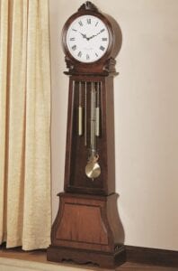 A grandfather clock is sitting on a table in front of a window.