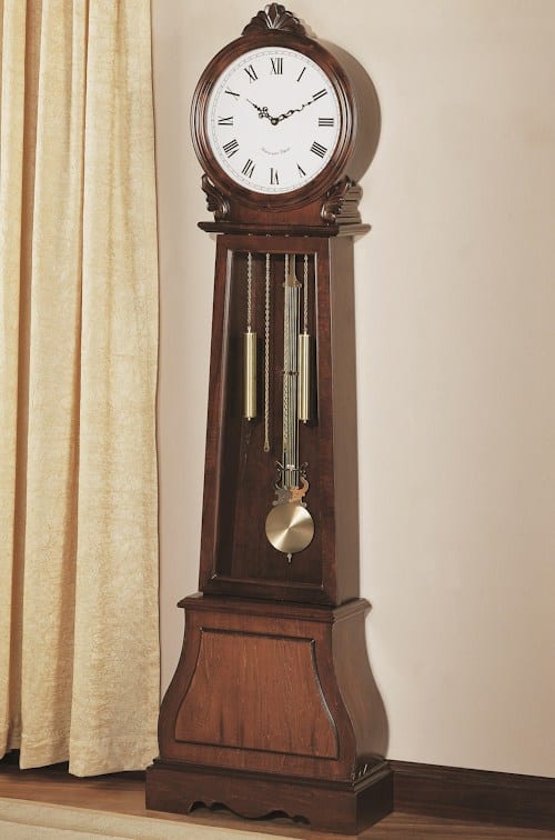 A grandfather clock is sitting on a table in front of a window.